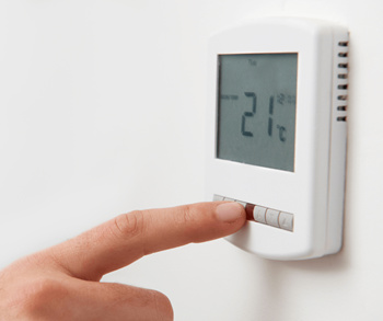 A person is pressing a button on a thermostat that shows 21 degrees.